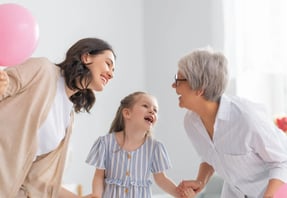 Madre, hija y abuela riendo juntas en casa, mostrando un momento de cariño familiar entre generaciones de madres.
