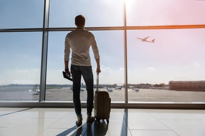 Hombre con maleta observando un avión despegar desde una ventana en el aeropuerto