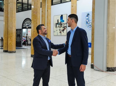 Dos hombres de traje estrechando manos en el vestíbulo de un edificio corporativo.