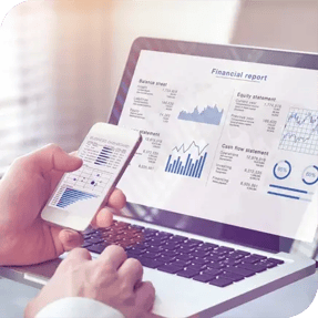 Persona revisando reportes financieros en un teléfono móvil y una computadora portátil