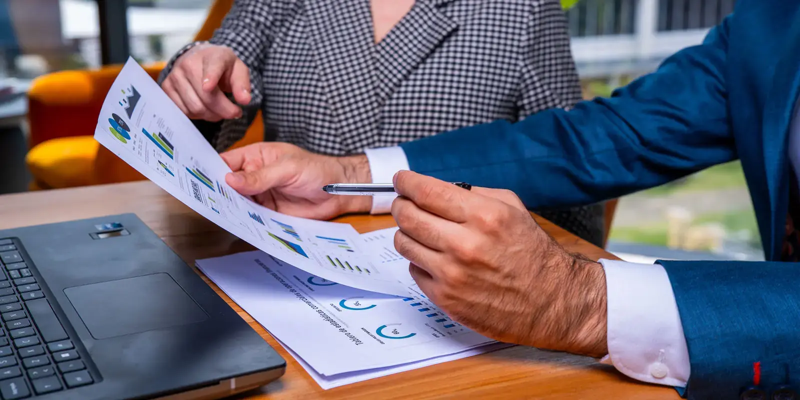 Personas revisando gráficos impresos en una mesa junto a una computadora portátil.