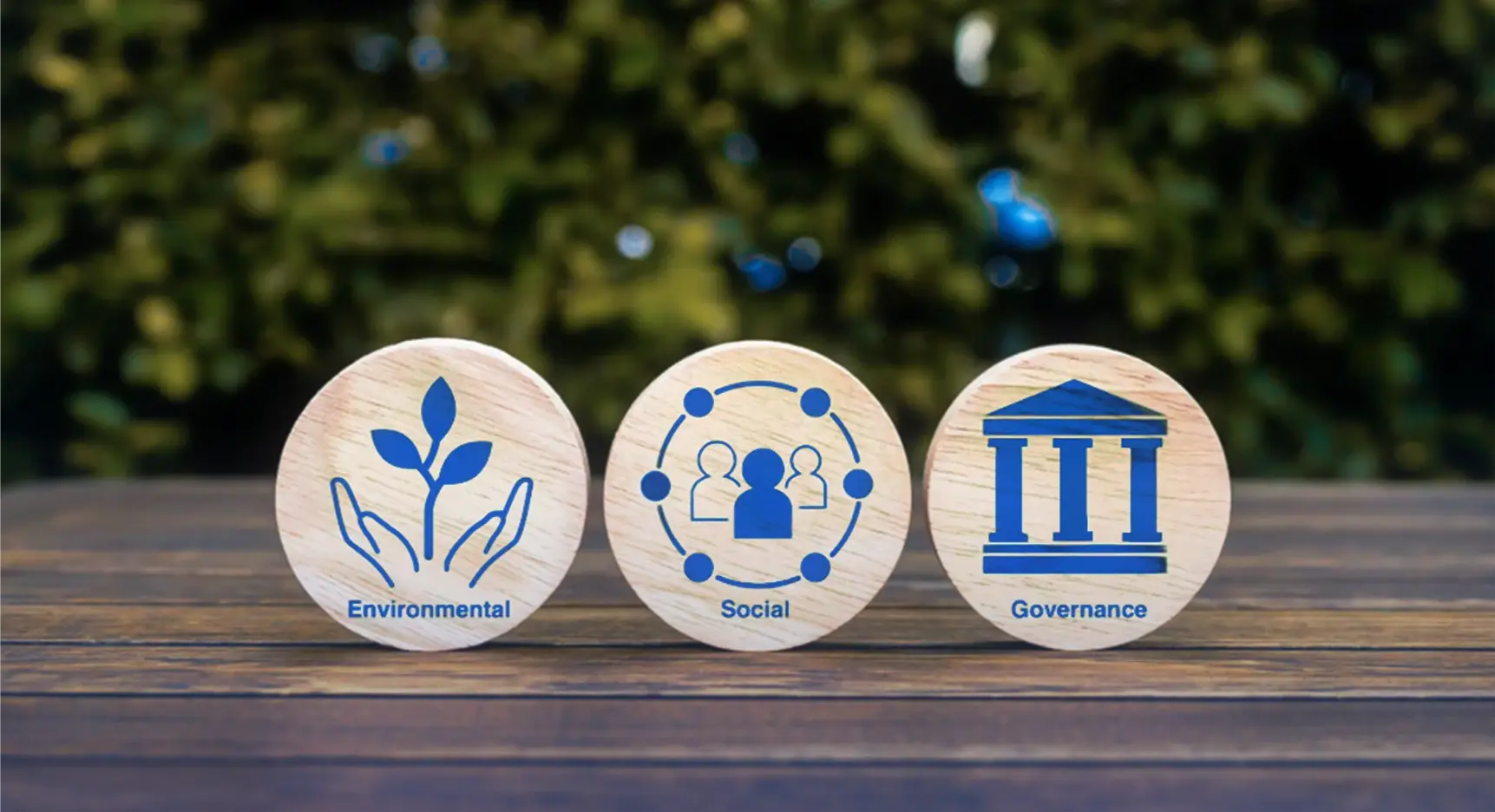 Tres fichas de madera con íconos que representan los pilares ESG: ambiental con una planta, social con figuras humanas conectadas y gobernanza con un edificio institucional.