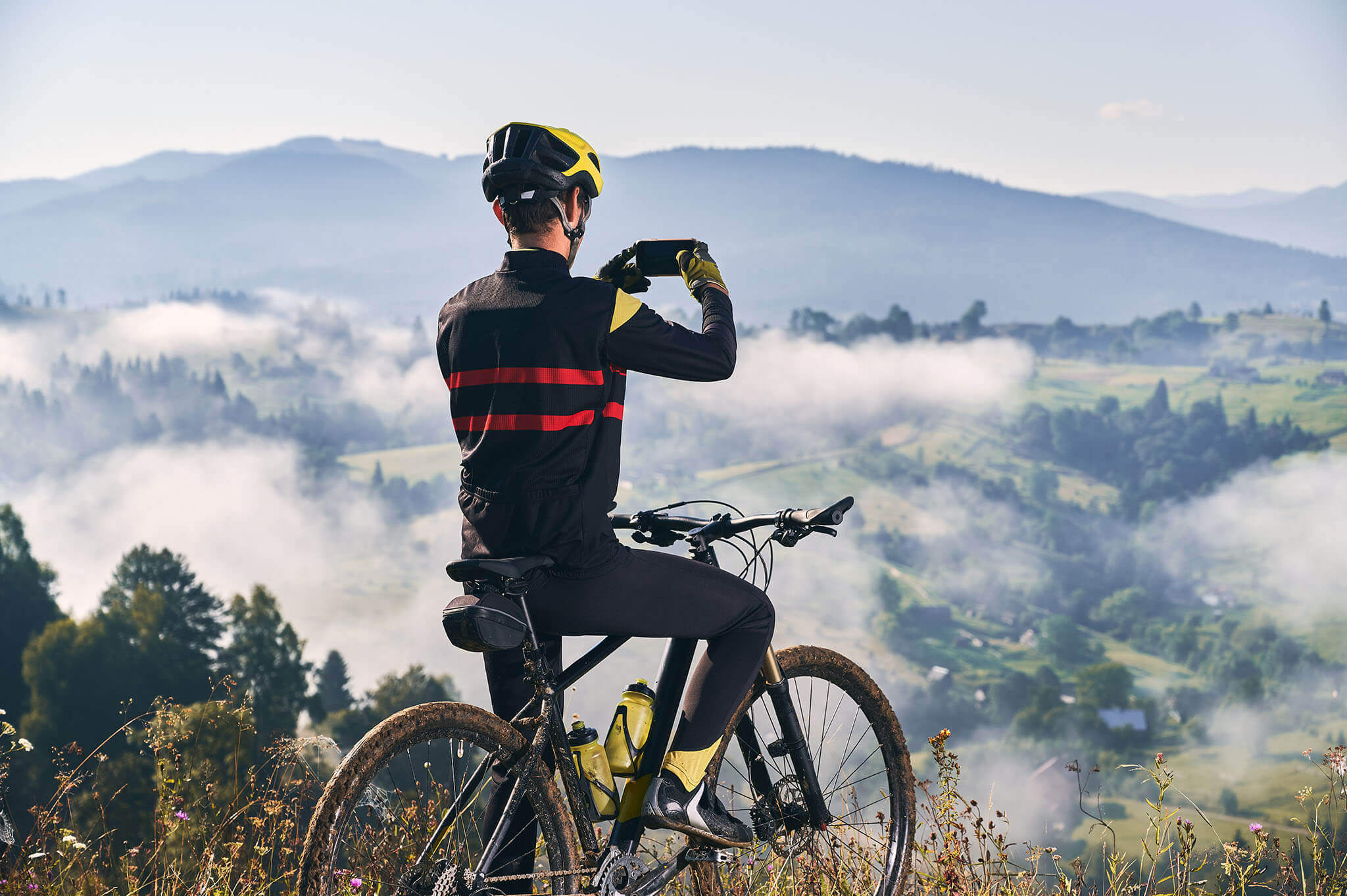 Ciclista con casco y ropa deportiva tomando foto de paisaje montañoso con neblina.