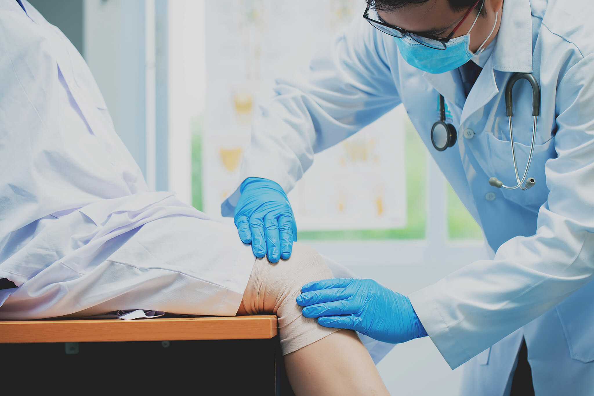 Médico revisando la rodilla vendada de un paciente en una consulta médica.