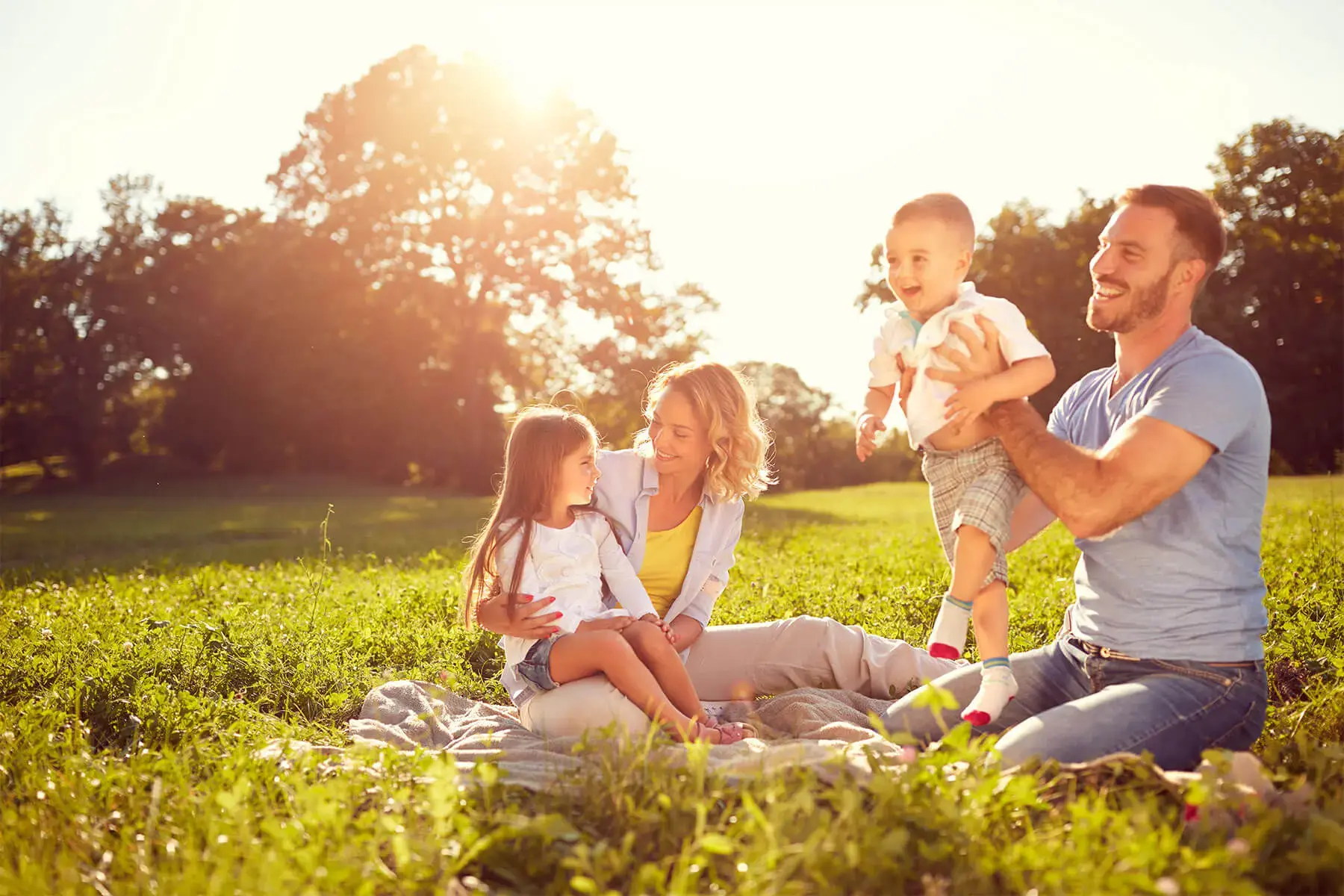 Familia disfrutando de un picnic en el campo al atardecer, sentados sobre una manta y rodeados de césped verde.