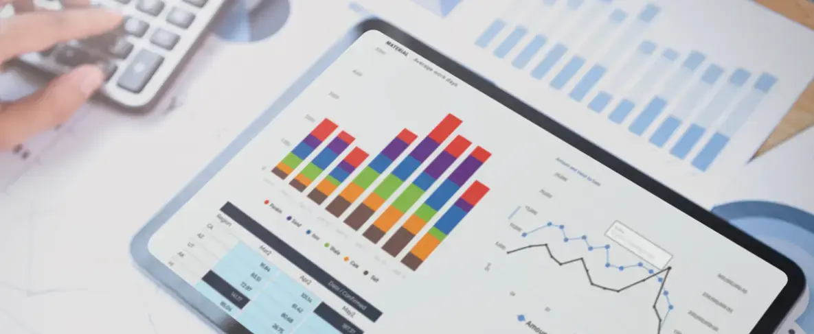 Mano usando una calculadora junto a una tablet que muestra gráficos de barras multicolores y líneas de rendimiento financiero.