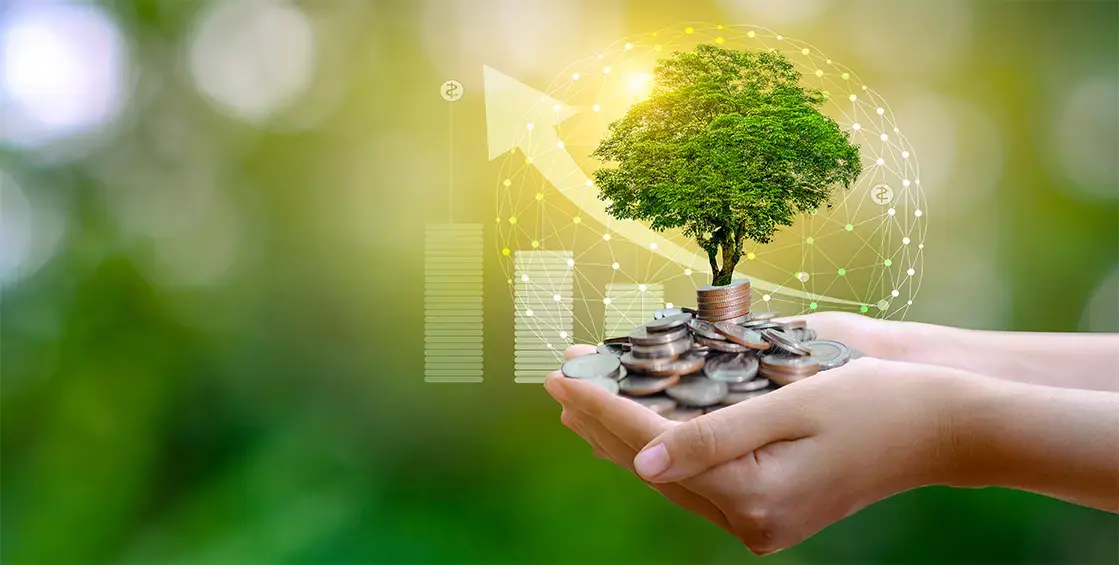 Manos sosteniendo monedas de las que crece un árbol, con gráficos financieros y conexiones digitales al fondo, simbolizando inversión sostenible.