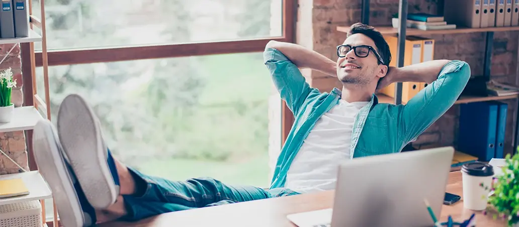 Hombre joven relajado en su escritorio con los pies sobre la mesa y manos detrás de la cabeza