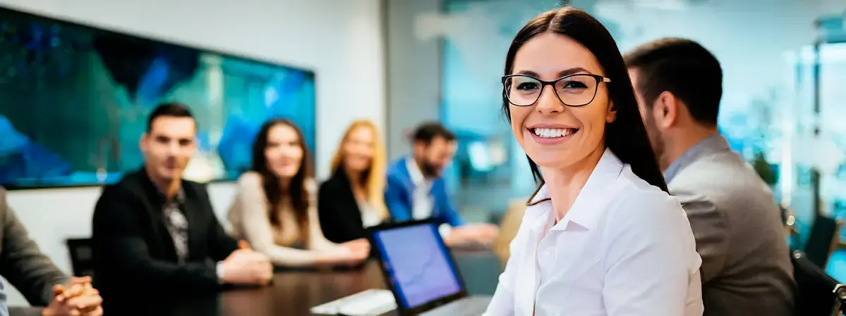 Mujer sonriendo en una sala de reuniones con compañeros de trabajo al fondo.