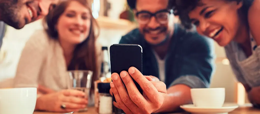 Grupo de amigos sonriendo mientras miran un teléfono móvil en una mesa de café.