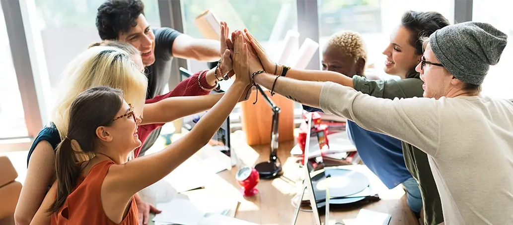 Grupo de jóvenes en una oficina celebrando con un gesto de manos unidas