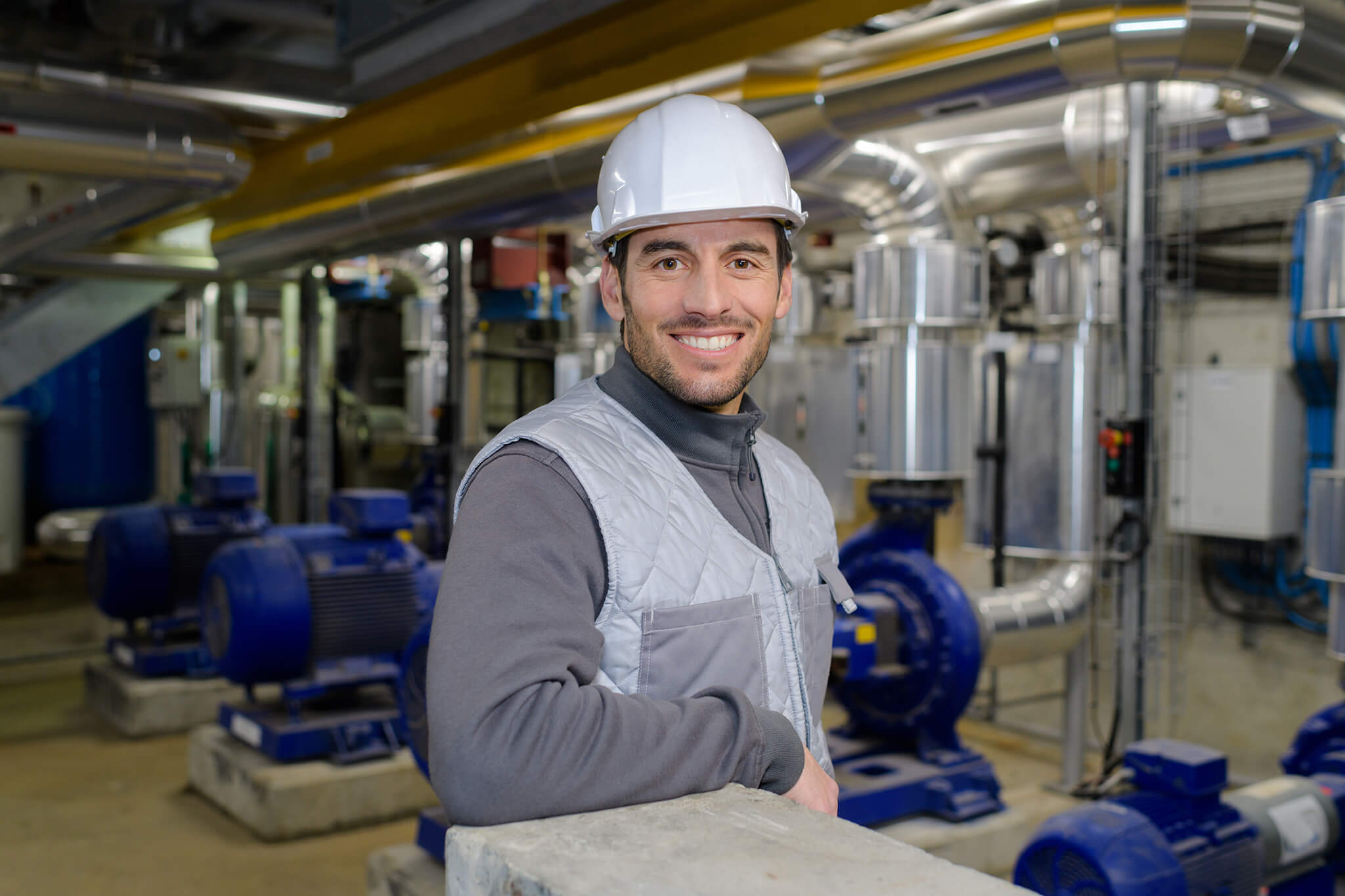 Trabajador industrial con casco de seguridad sonriendo en una planta de maquinaria.