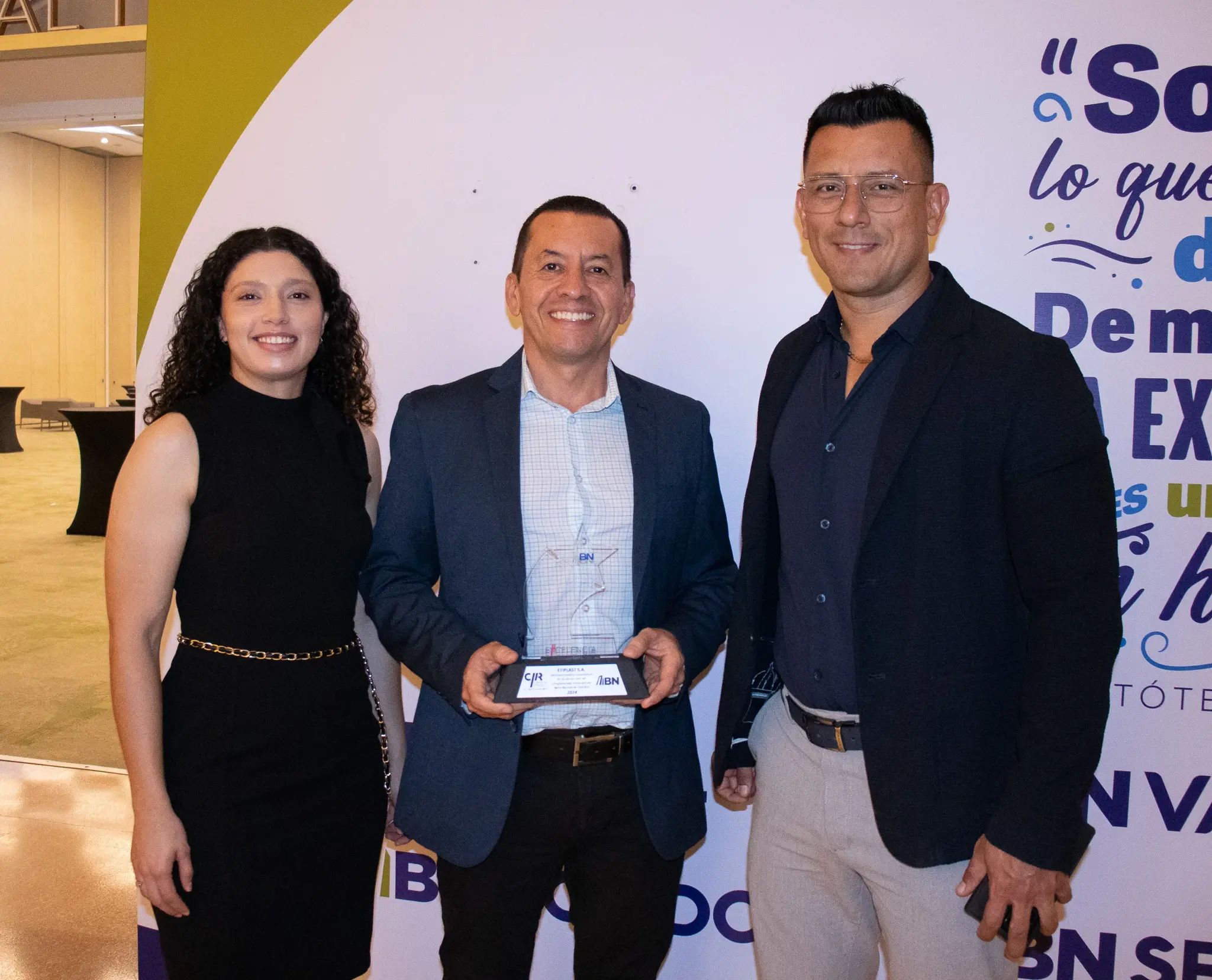 Grupo de tres personas posando en un evento, una mujer y dos hombres, uno de ellos sosteniendo un trofeo con logotipos de BN y CICR.