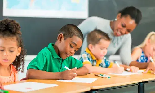 Niños escribiendo en clase junto a su maestra.