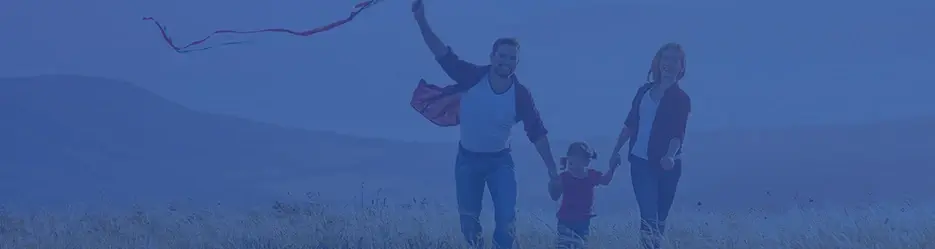 Familia caminando en el campo mientras vuelan una cometa en un día soleado.