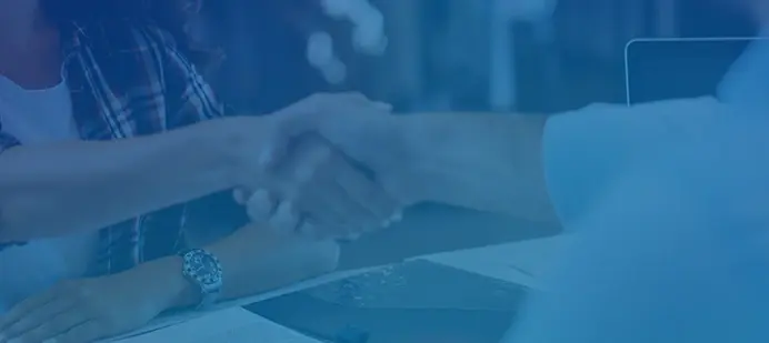 Dos personas dándose la mano sobre un escritorio en señal de acuerdo