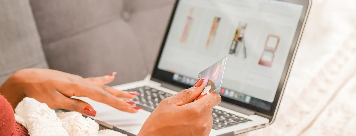 Persona haciendo compras en línea con tarjeta de crédito frente a una laptop.