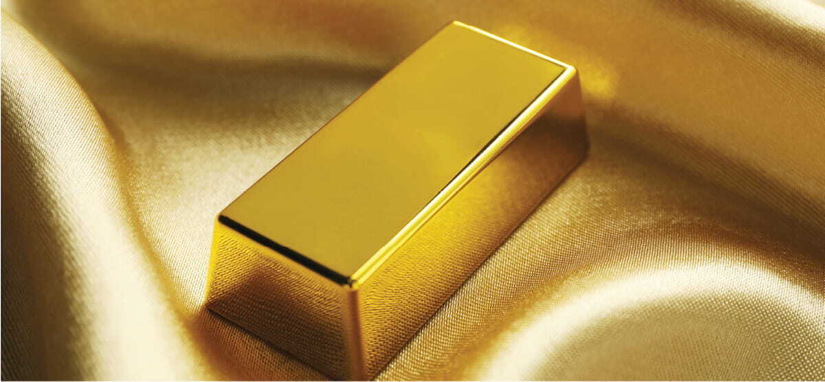 Lingote de oro brillante y pulido colocado sobre una elegante tela de seda dorada con pliegues suaves.
