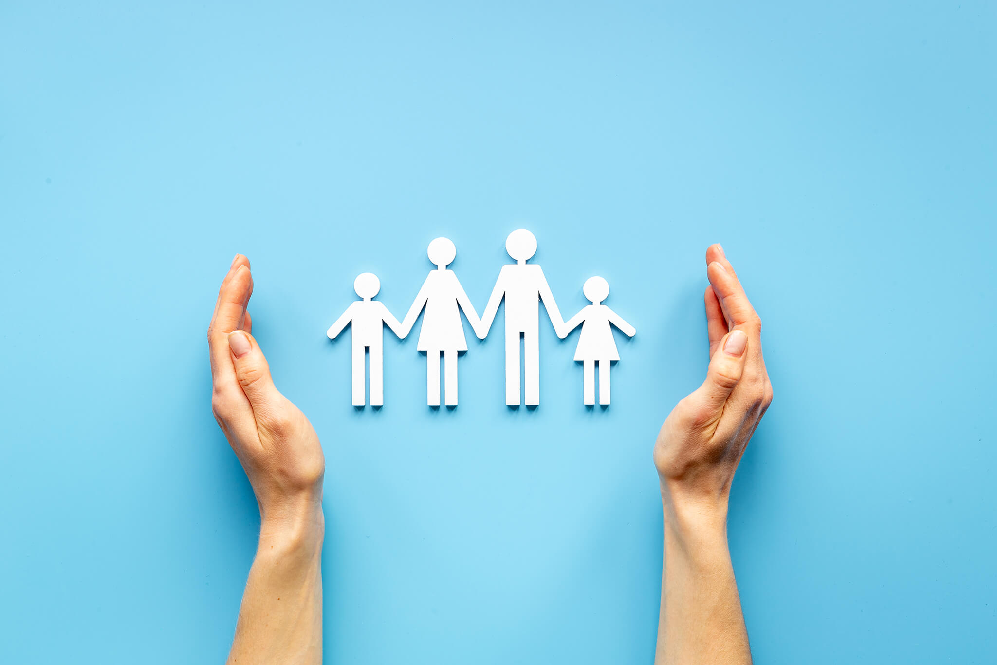 Manos protegiendo una figura recortada de una familia sobre fondo azul.