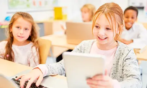 Niña usando una tablet en el aula, acompañada de compañeros.