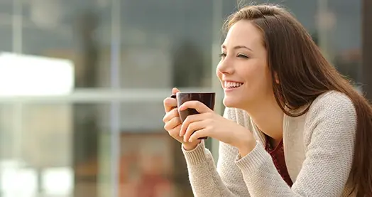 Mujer joven sonriendo mientras sostiene una taza de café al aire libre