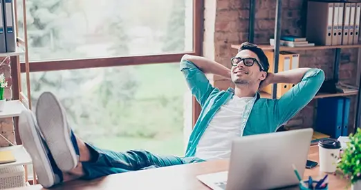 Hombre joven relajado en su escritorio con los pies sobre la mesa y manos detrás de la cabeza
