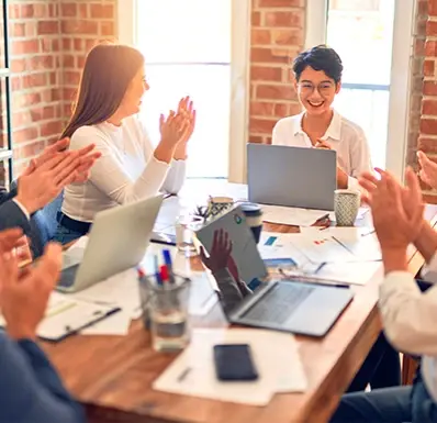 Equipo de trabajo aplaudiendo a una mujer frente a su laptop en una reunión