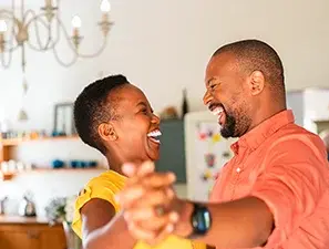 Pareja feliz bailando en casa mientras sonríen y se miran.