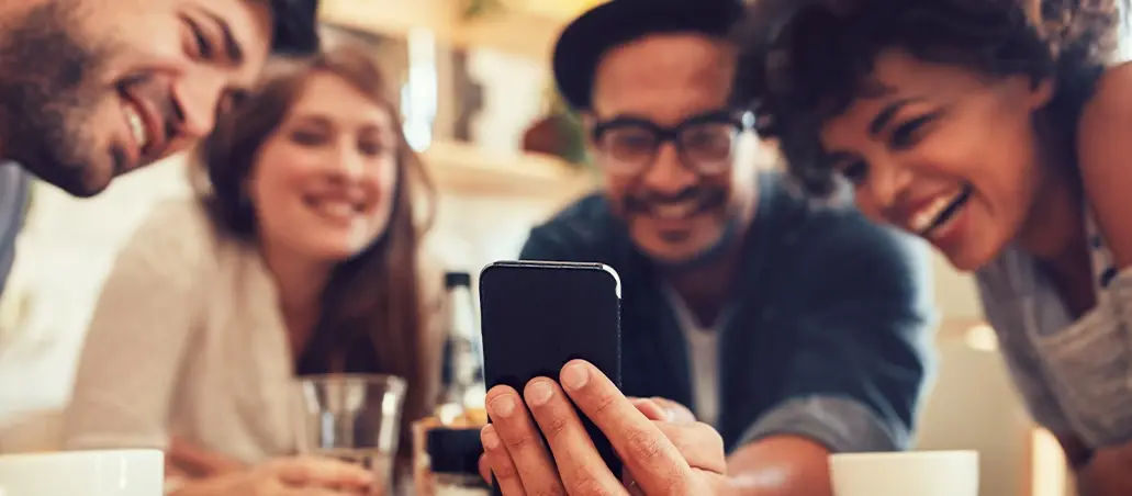 Grupo de amigos sonriendo mientras miran la pantalla de un teléfono móvil