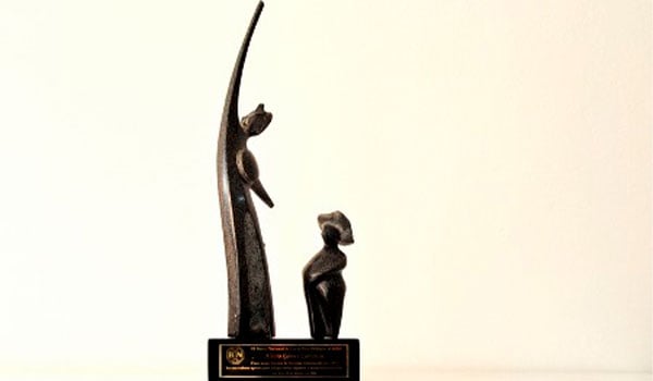 Estatuilla de bronce con figuras estilizadas sobre base con placa de reconocimiento.